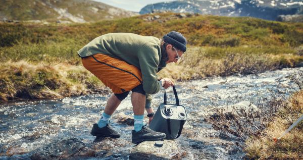 Personne remplissant son réservoir d'eau dans un ruisseau en montagne