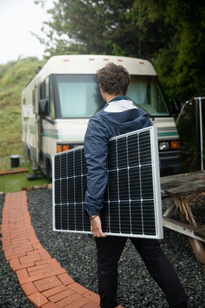 Homme tenant un panneau solaire devant son camping car